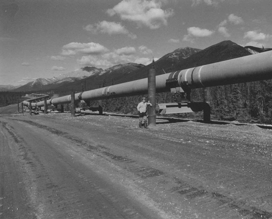 An engineer standing next to a section of the trans-Alaska pipeline.