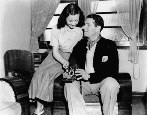 Sir Laurence Olivier and Lady Olivier (Vivien Leigh) on a short holiday at the Gold Coast after touring with the Old Vic Company in Hobart. Sir Laurence is elegantly dressed in a jacket, flannels and a open-necked shirt with a cravat. Lady Olivier is wear